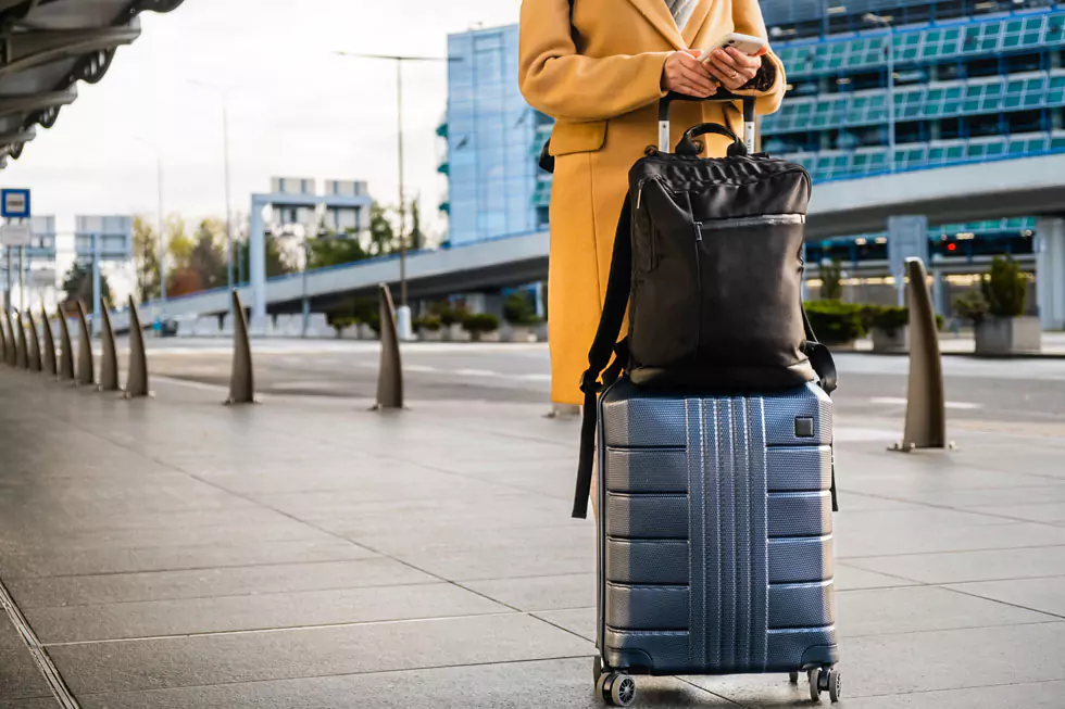 Frau am Flughafen wartet auf ein Taxi und tippt auf dem Smartphone