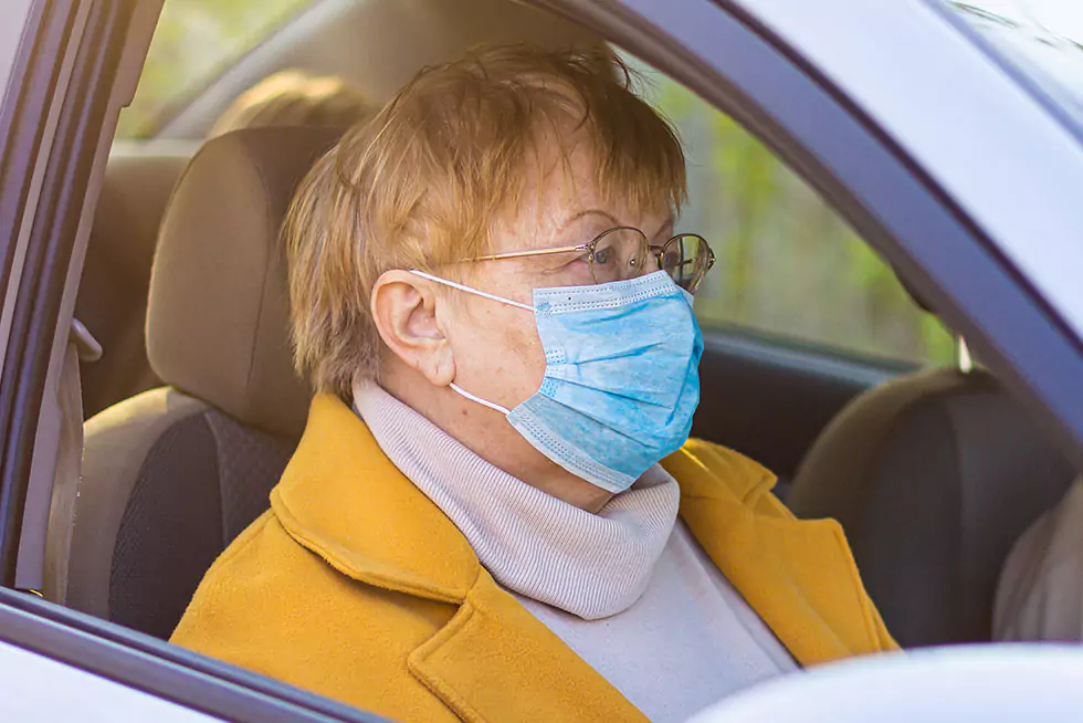 ältere Dame mit Gesichtsmaske sitzt auf dem Beifahrersitz eines Autos
