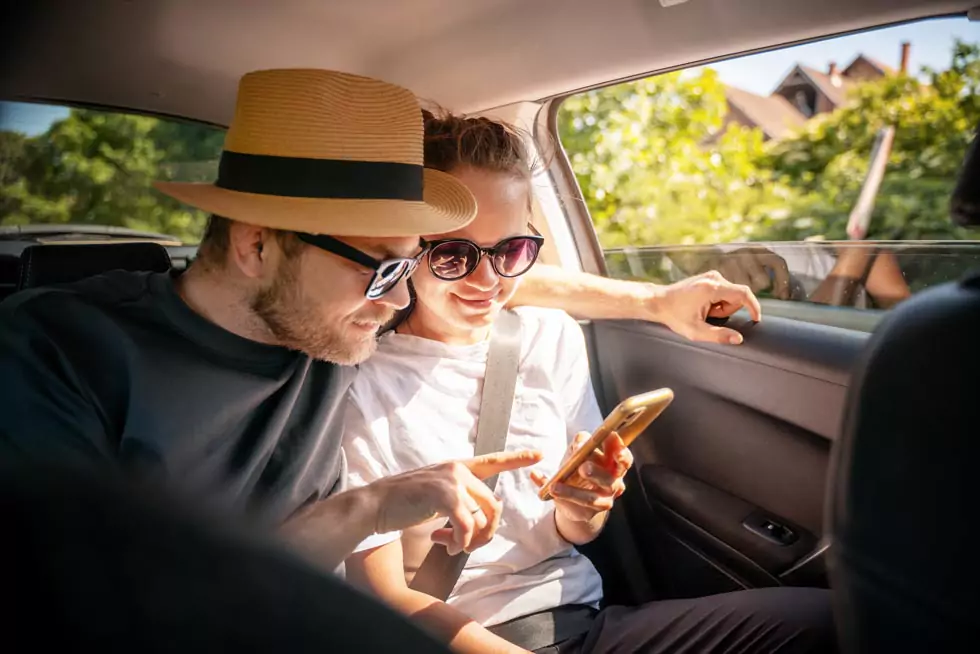 junges Paar in einem Taxi schaut auf ein Smartphone